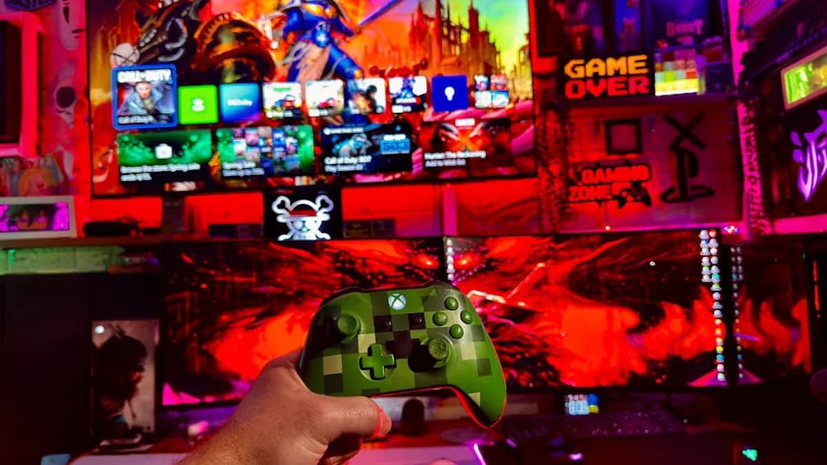 Person holding a video game controller in front of screens.