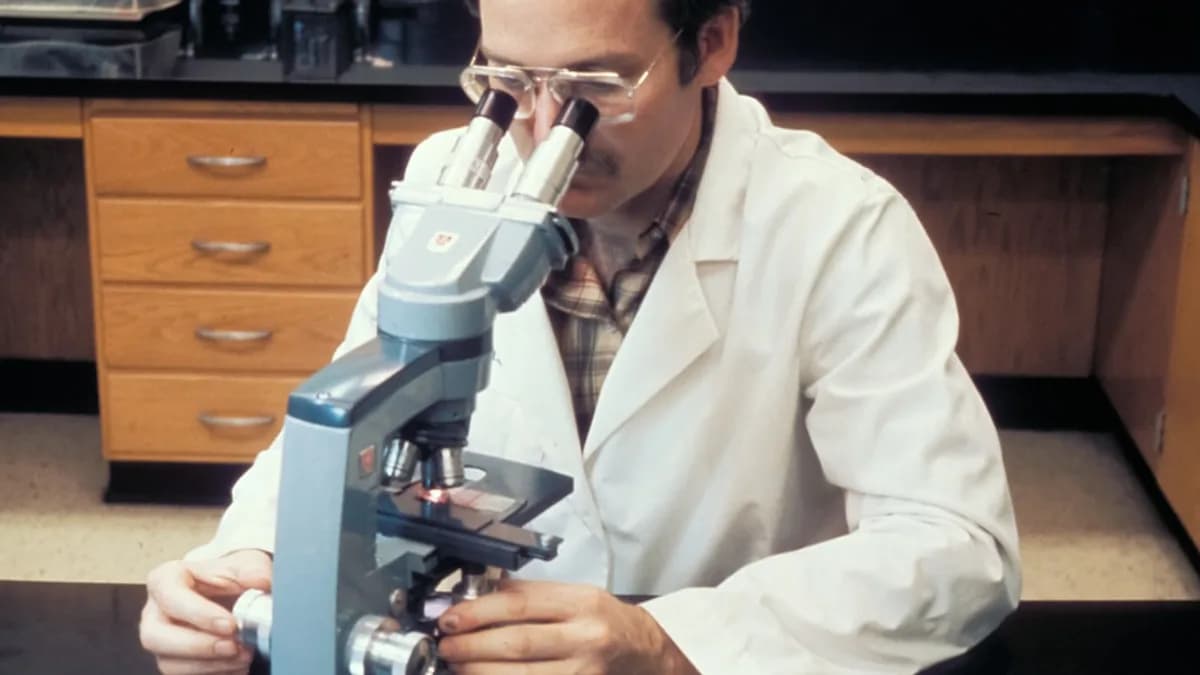 a man in a lab coat looking through a microscope