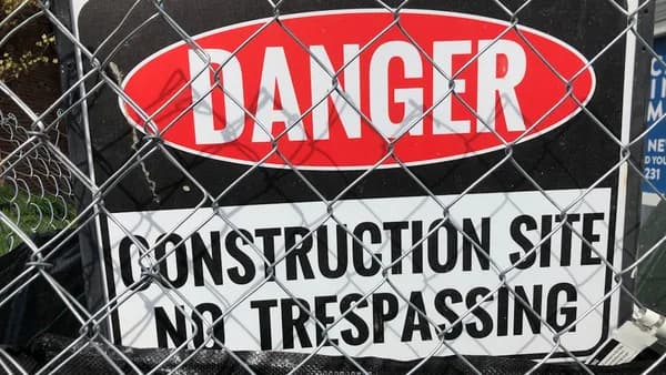 a sign on a fence that says danger construction site no trespassing