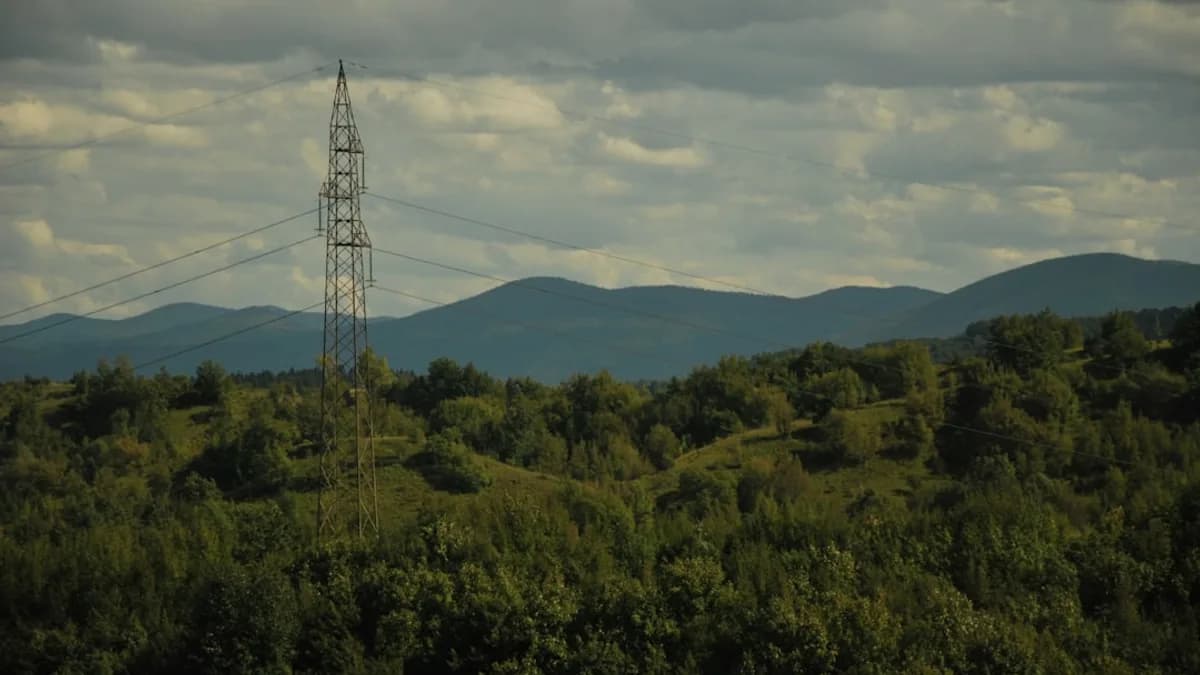 Tall pylon stands against rolling hills and cloudy sky.