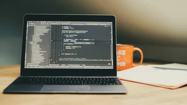 Laptop displaying code with an orange mug nearby