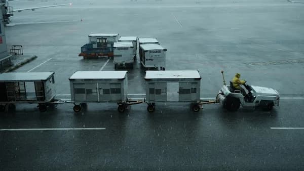 A man is sitting on a luggage cart in the rain