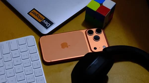 Laptop, phone, keyboard, headphones, and puzzle cube on desk.