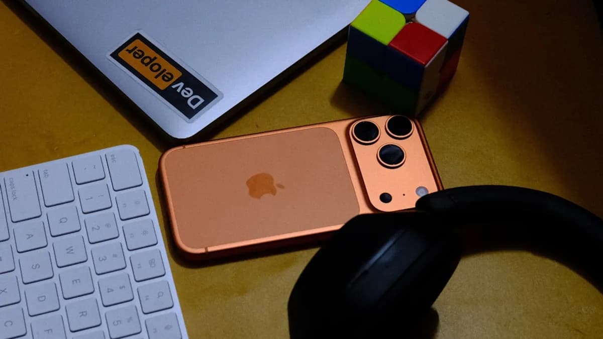 Laptop, phone, keyboard, headphones, and puzzle cube on desk.
