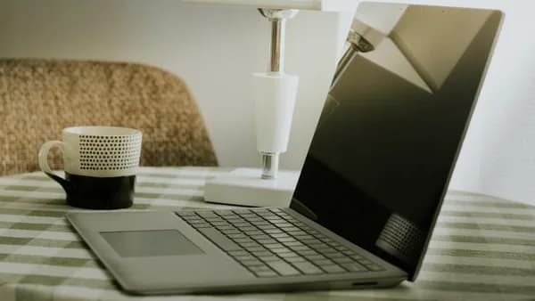 Laptop and coffee cup on a checkered tablecloth.