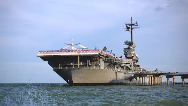 An aircraft carrier docked at a pier by the sea.
