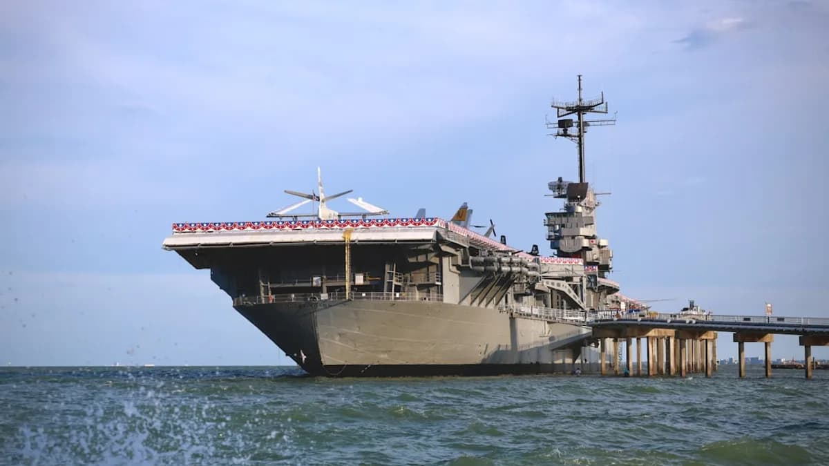 An aircraft carrier docked at a pier by the sea.