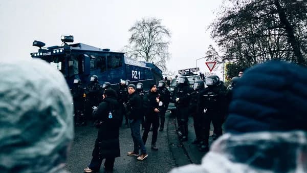 Riot police officers stand in formation near a vehicle.