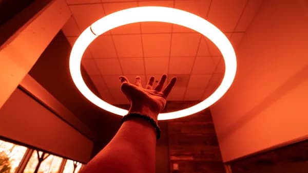 person reaching round turned-on fluorescent lamp in room