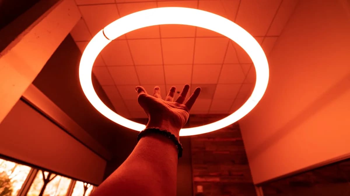 person reaching round turned-on fluorescent lamp in room