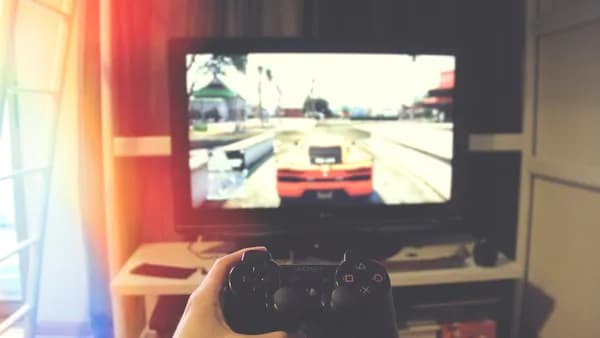 person holding Sony PS3 controller in front of flat screen monitor