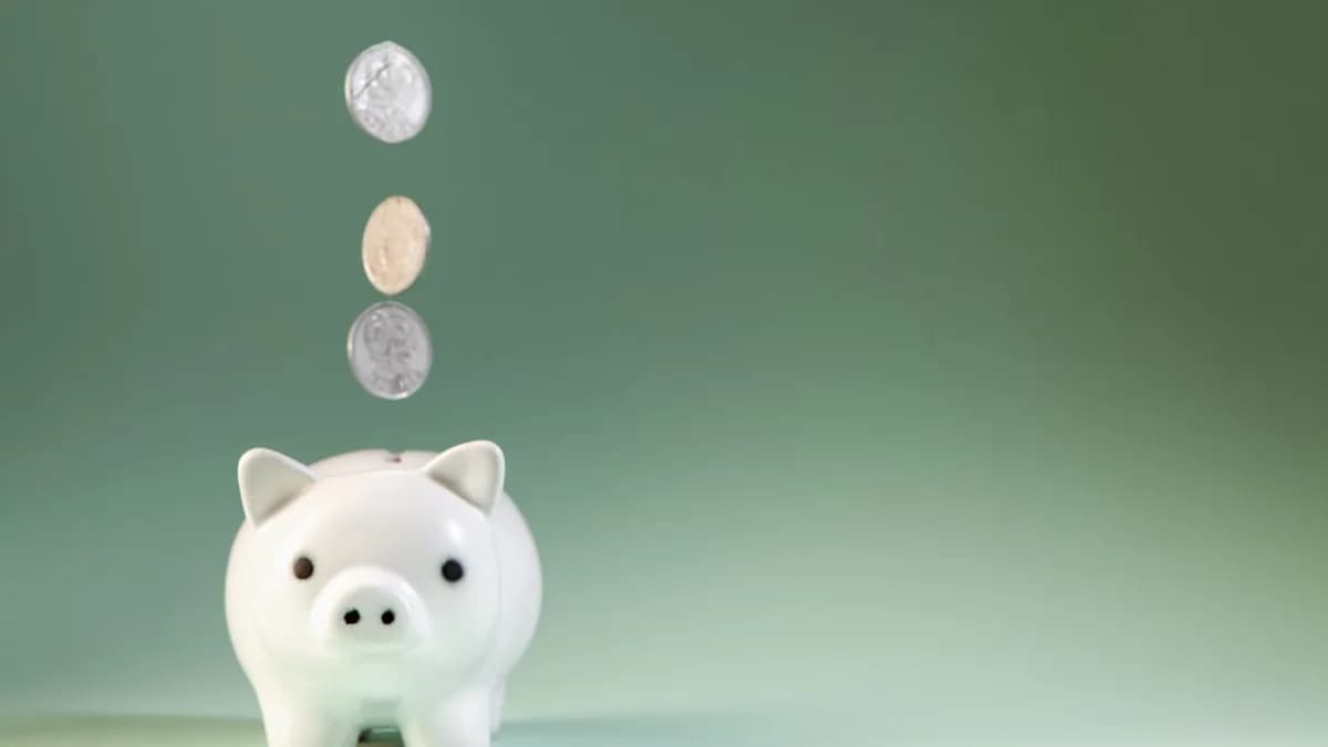 Coins falling into a white piggy bank.