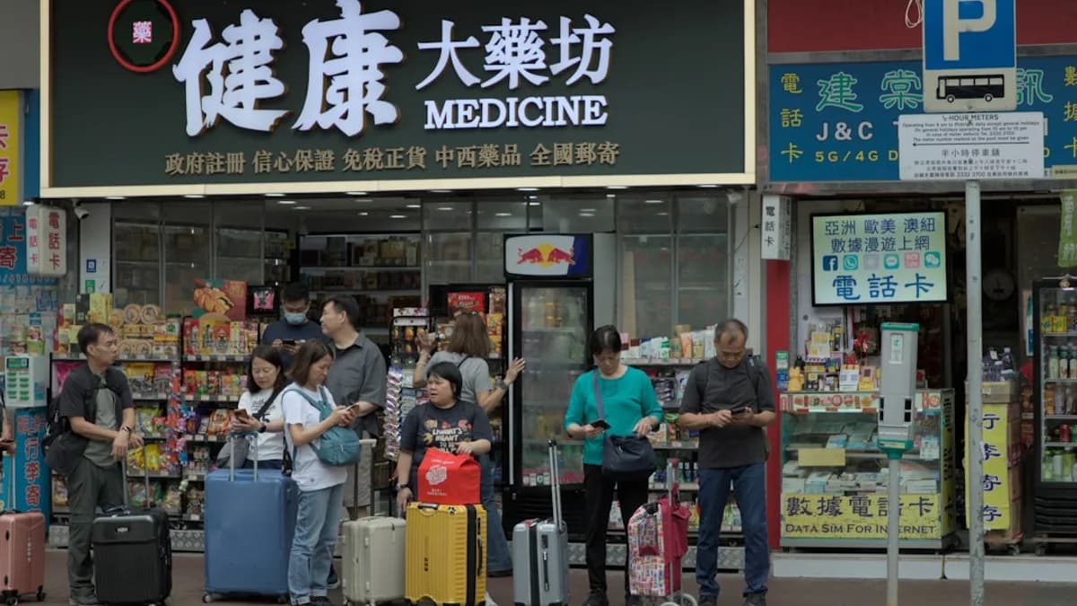 People with luggage wait outside a medicine shop.