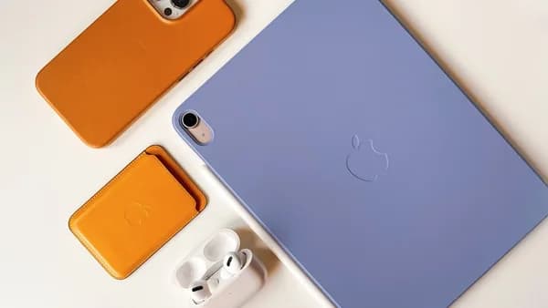 Orange phone case, wallet, and white earbuds next to tablet.