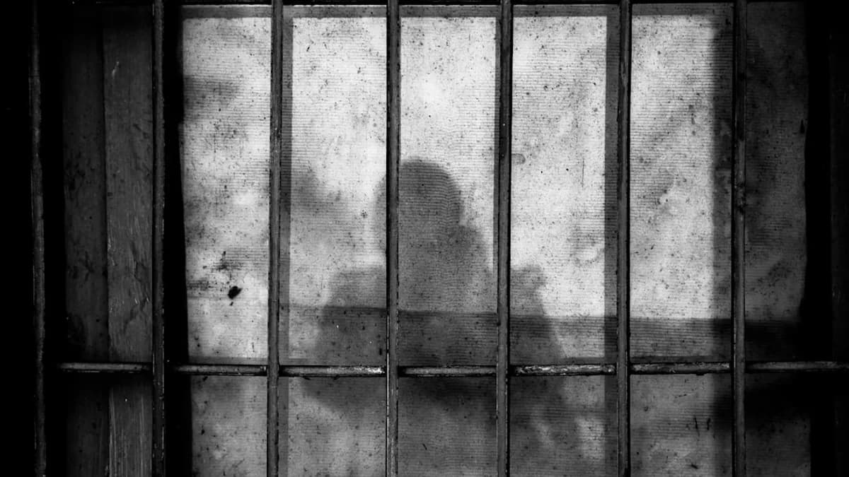 a shadow of a person behind bars in a jail cell