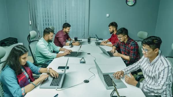 a group of people sitting around a table with laptops