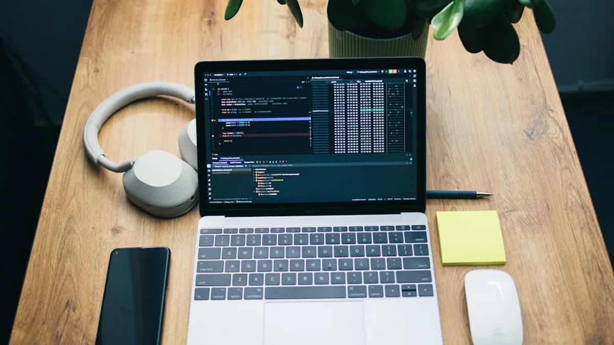 Laptop with code, headphones, phone, and mouse on desk.
