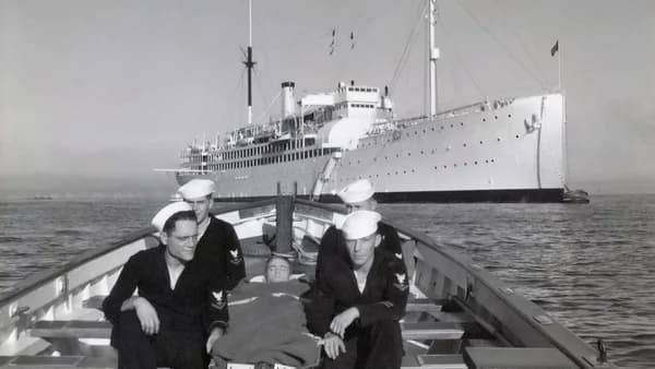 Sailors in a boat with a ship behind them.