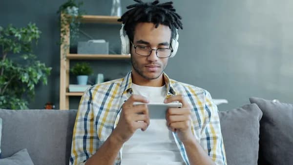 Man wearing headphones plays game on smartphone.
