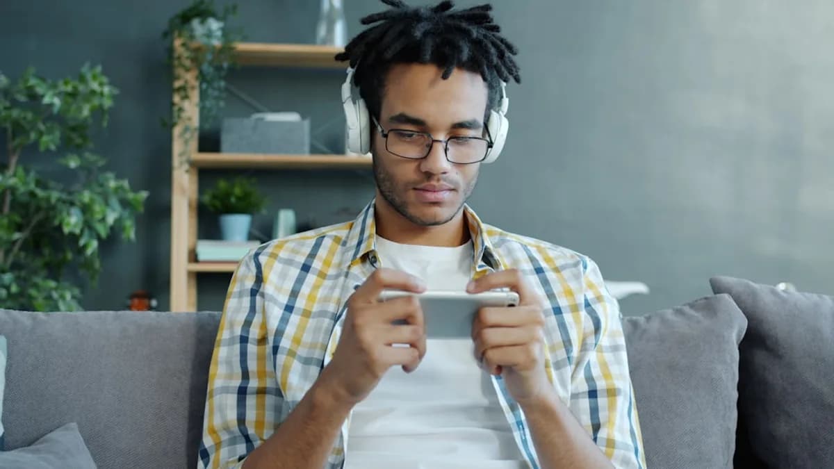 Man wearing headphones plays game on smartphone.