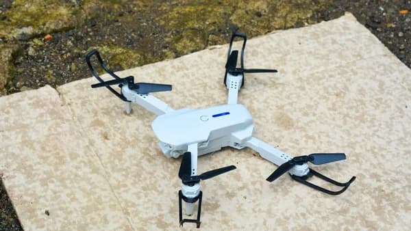 A white drone rests on a textured surface.
