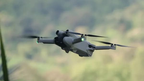 a small gray helicopter flying over a lush green hillside