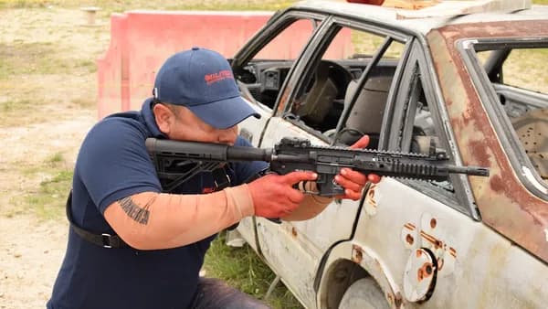 a man holding a rifle in front of a car