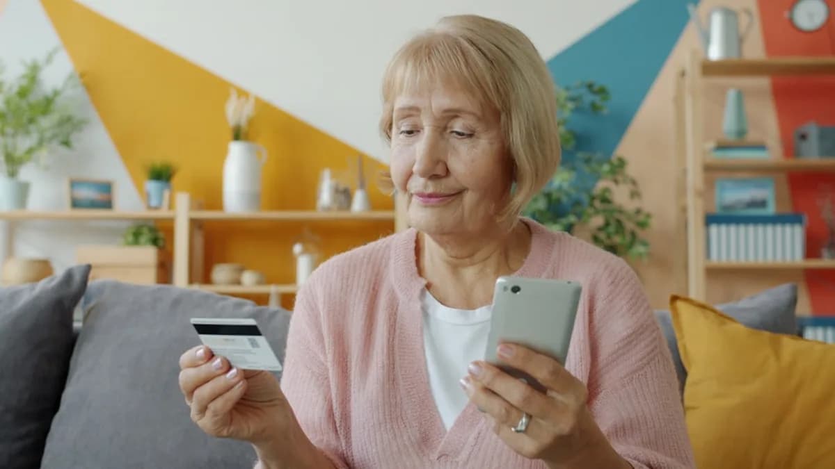 Elderly woman holding credit card and smartphone.