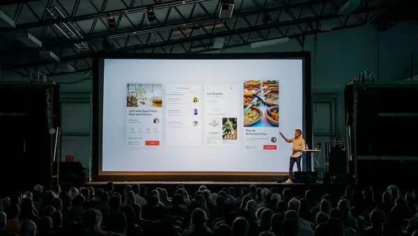 person discussing while standing in front of a large screen in front of people inside dim-lighted room