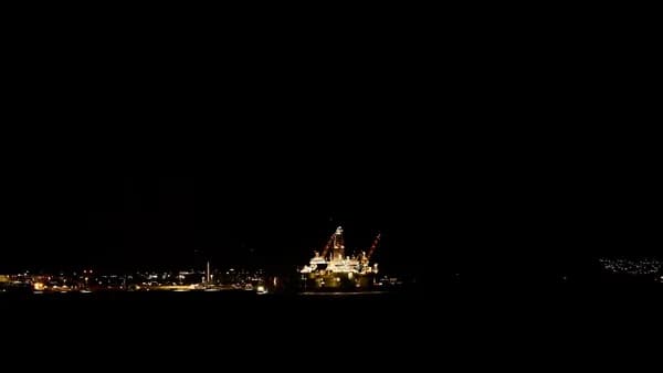 Offshore oil rig illuminated at night with city lights.