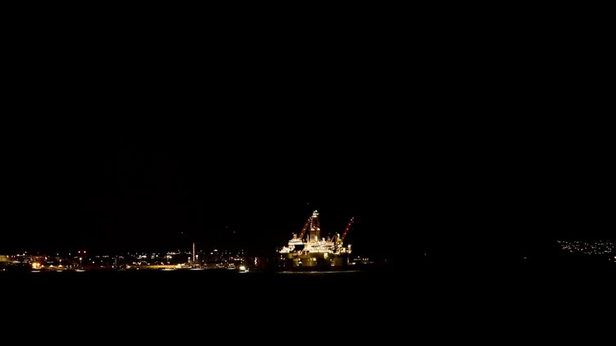 Offshore oil rig illuminated at night with city lights.