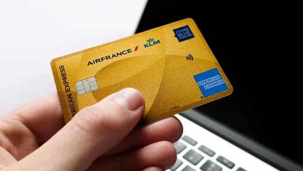 Hand holding a gold american express card near laptop.