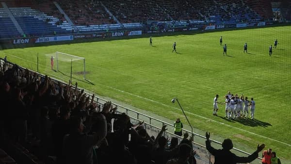 Soccer players celebrate on a grassy field with cheering fans.