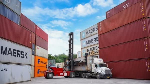 Forklift moving shipping containers at a port.