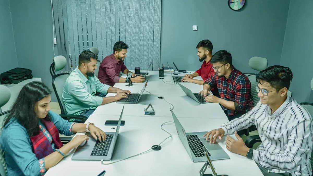 a group of people sitting around a table with laptops