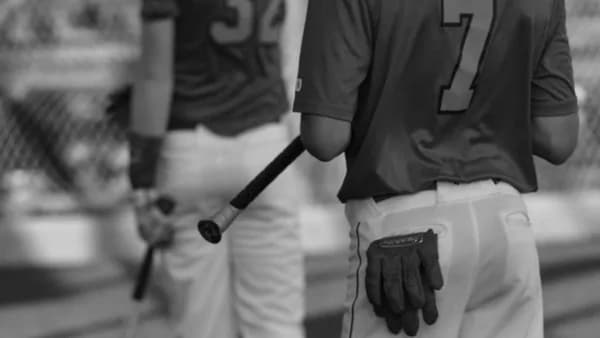 grayscale photo of man in black crew neck t-shirt and white pants holding baseball bat