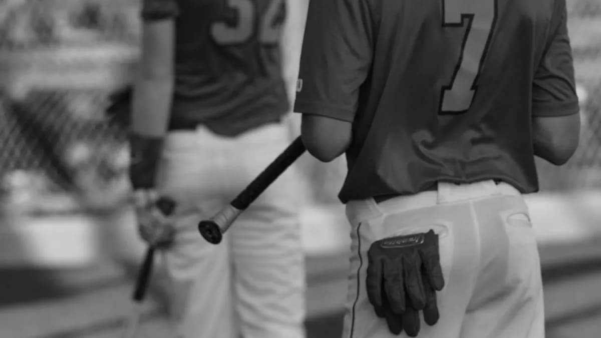 grayscale photo of man in black crew neck t-shirt and white pants holding baseball bat