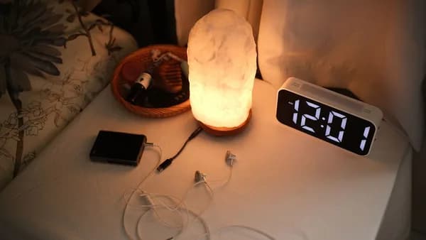 Nightstand with a lamp, clock, and chargers.