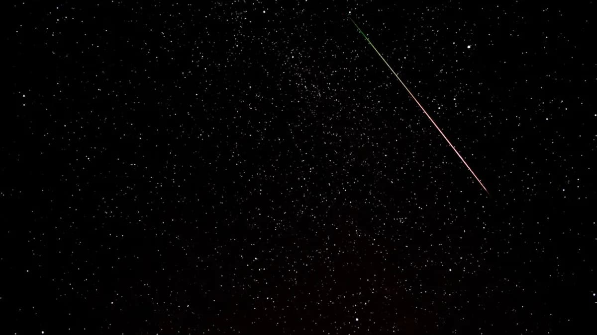 A meteor streaks across a starry night sky.