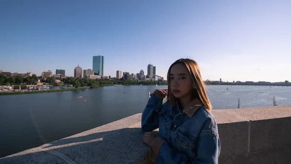 woman in blue denim jacket sitting on gray concrete pavement near body of water during daytime