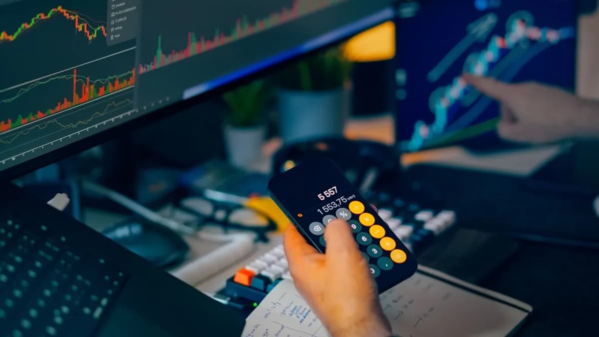 Trader analyzing stock market charts on computer screens with calculator.