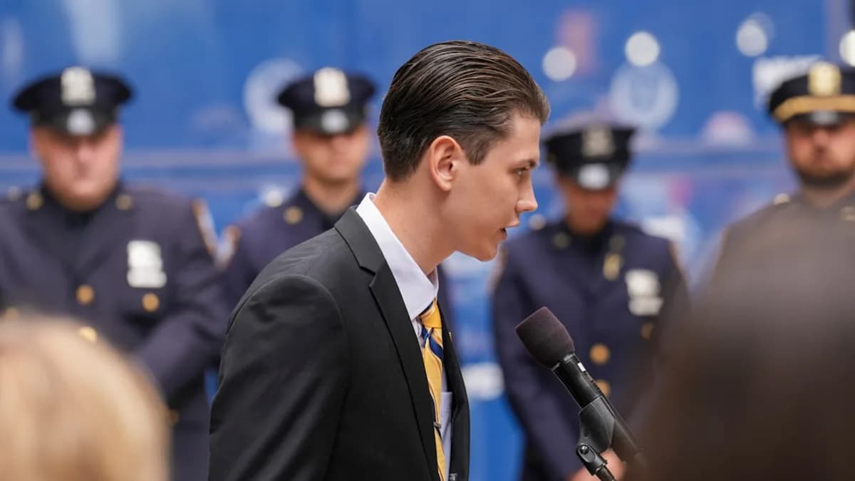 Man in suit speaks at podium with police officers behind.
