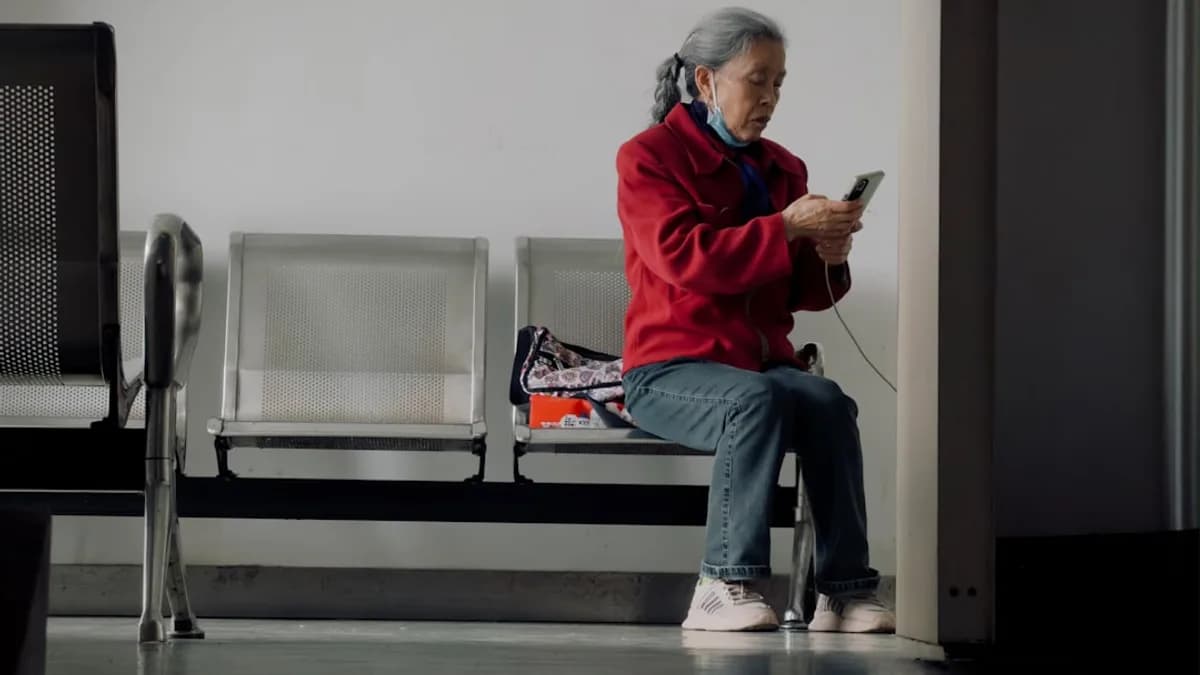 Elderly woman in red jacket uses smartphone while sitting.