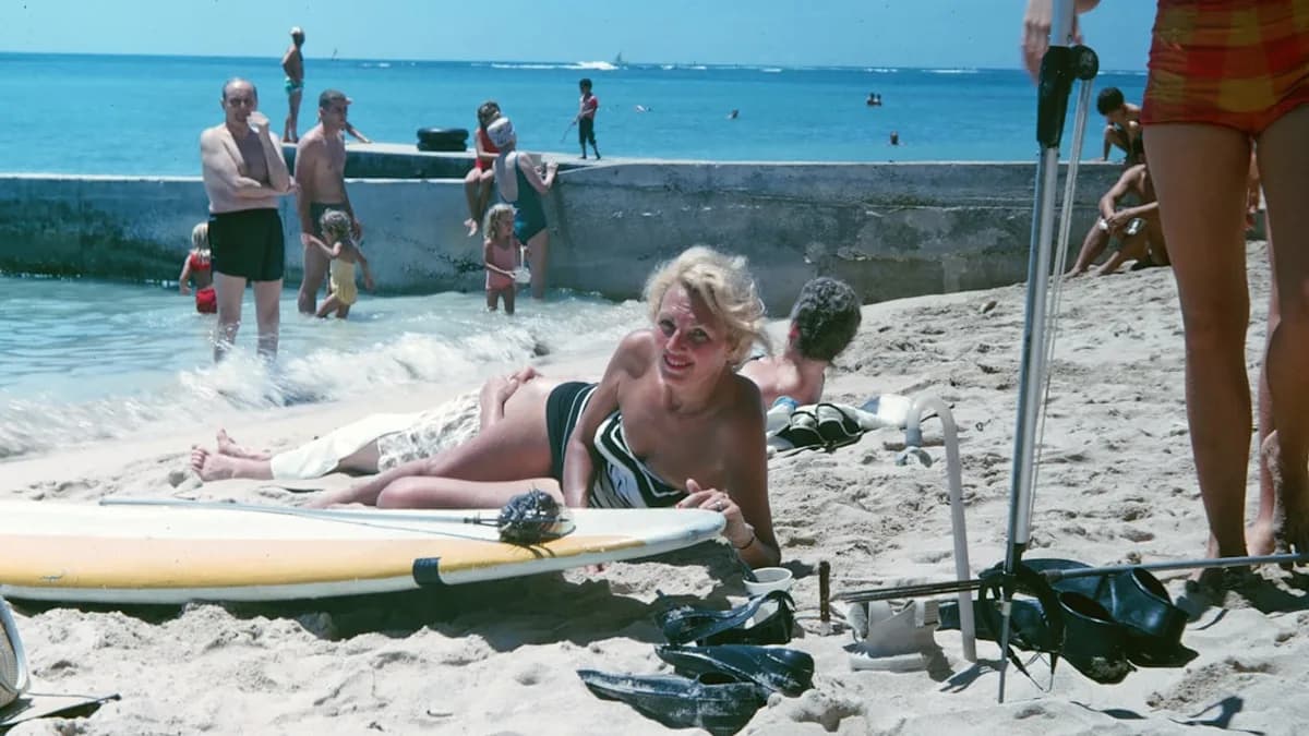 woman sunbathing near white and yellow surfboard and other people standing on beach