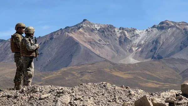 Two soldiers stand on a rocky outcrop overlooking mountains.