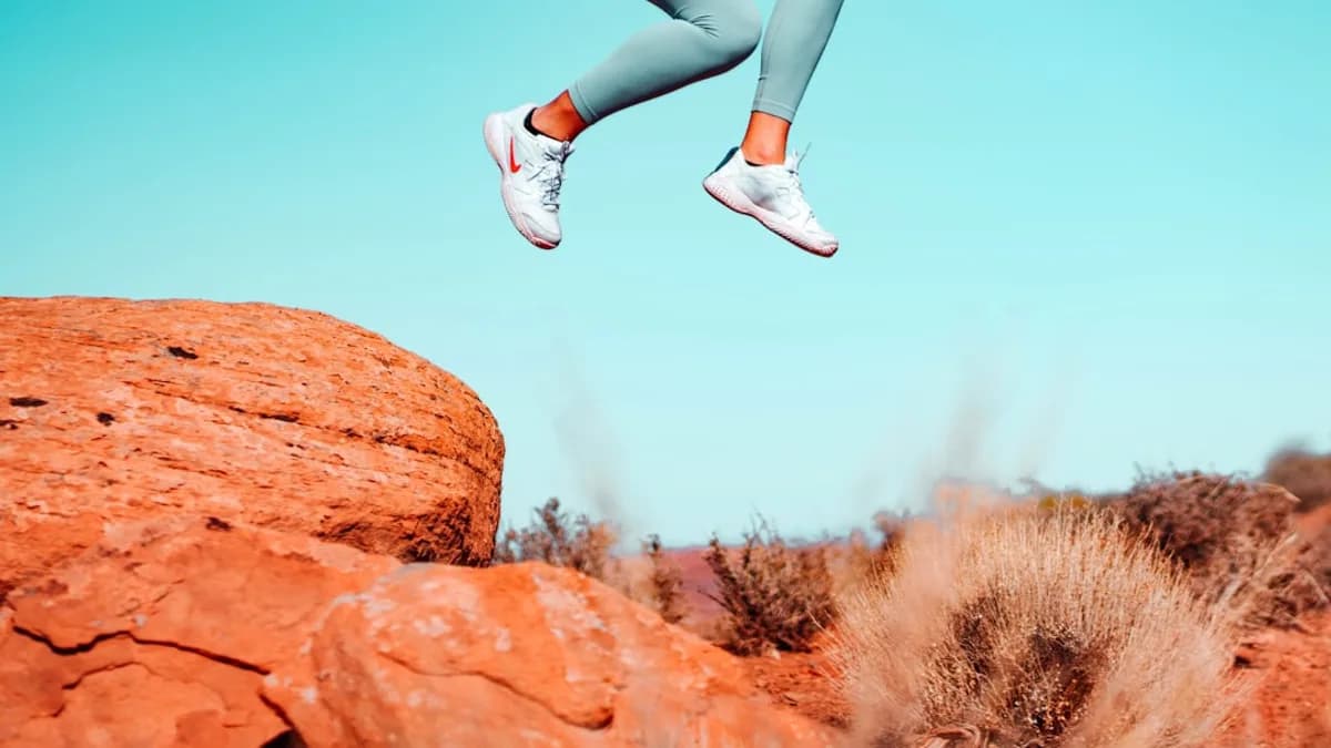 woman in blue denim jeans and white sneakers sitting on brown rock during daytime