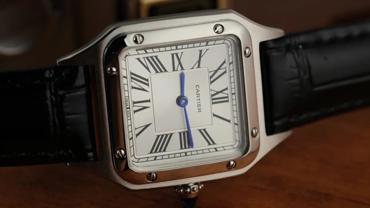 A silver square watch with a black leather strap.