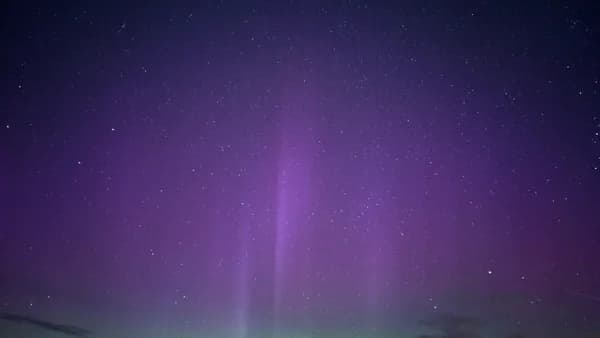 A purple and green light shines in the night sky