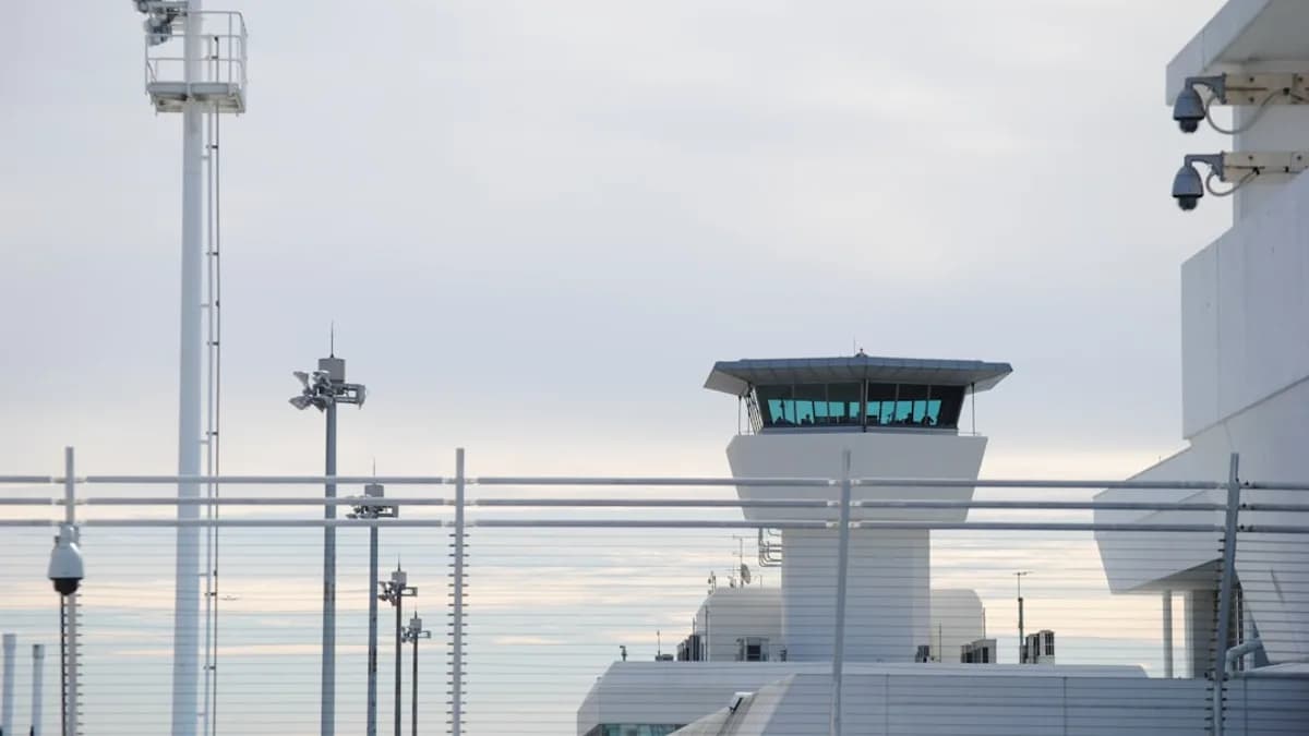 An airport control tower stands against a cloudy sky.