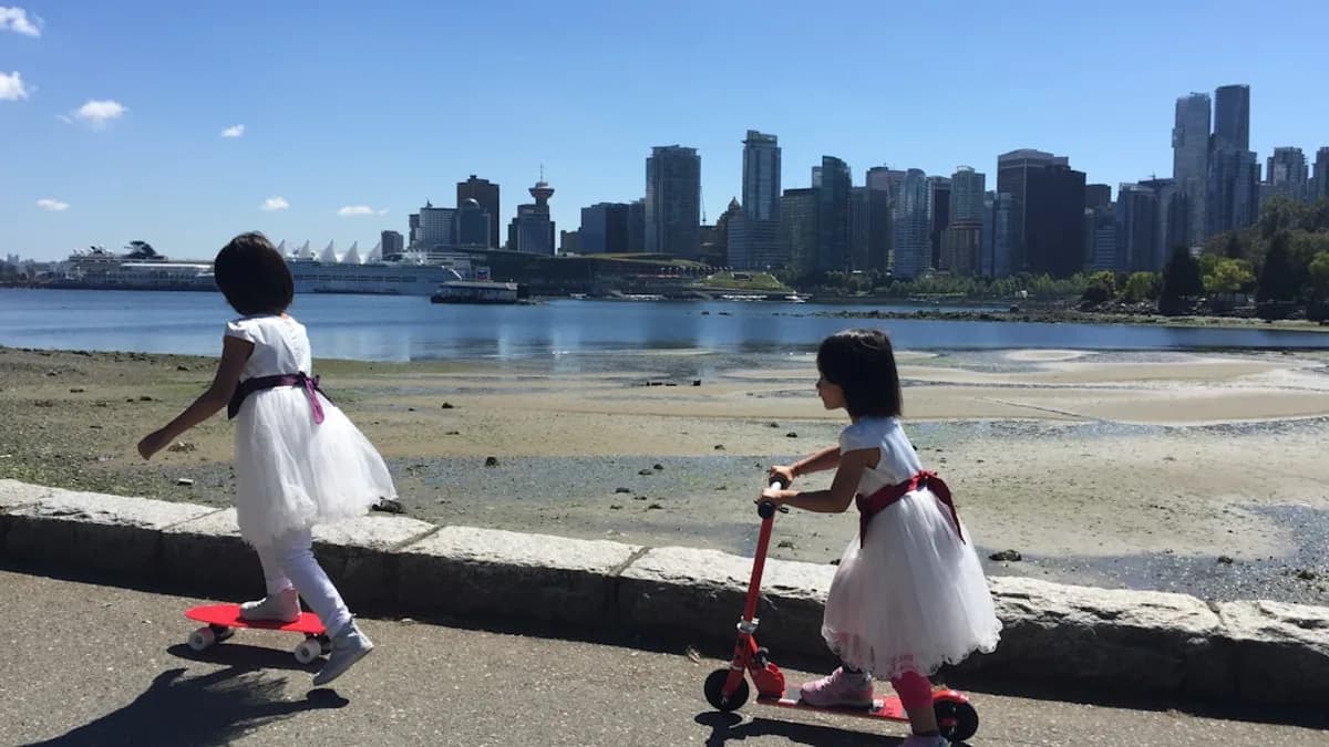 two little girls in dresses are riding scooters by the water